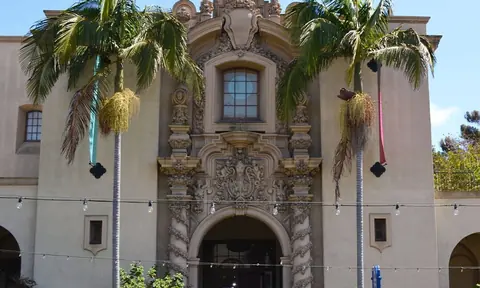 两棵棕榈树之间是一座浅色历史建筑的雕花拱门立面。