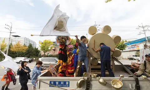 户外场地中多人围绕车载装置作业，旁边有大型圆形与兽形构件。