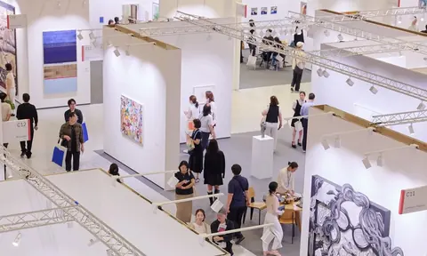 俯瞰明亮展厅内的多排白色展位、墙上作品与往来观众。