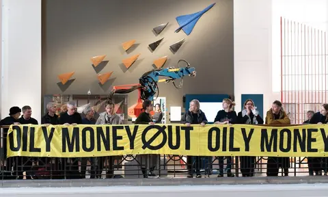 博物馆大厅内一排人举着写有 OILY MONEY OUT 的黄色横幅。