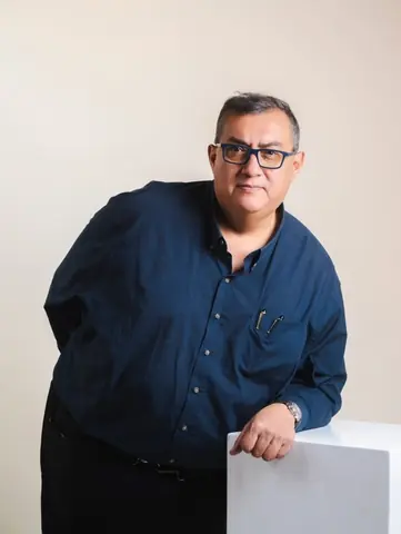 策展人 Cuauhtémoc Medina 戴黑框眼镜倚靠白色展台