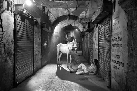 MW Wasif 的黑白作品画面:石质通道中的人物仰望上方白马