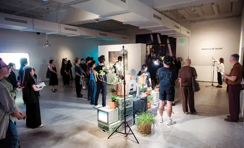 Mandeville Art Gallery 展厅内观众围绕植物与显示设备组成的装置聆听讲话
