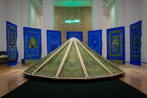 Mounira Al Solh 的绿色雕塑与蓝色织物作品陈列在展厅中