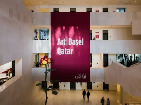 2026 年首届 Art Basel Qatar 场馆内景,白色中庭悬挂酒红色展会标识